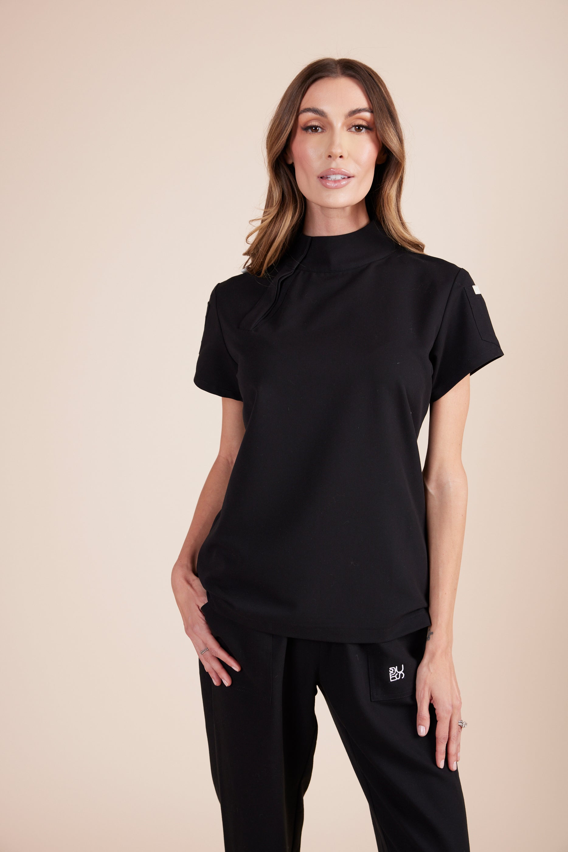Jackie Scrub Top in Black by DUES – luxury scrub top sewn in the USA, featuring contrast key loops, side splits, and high-stretch panels for comfort and mobility.