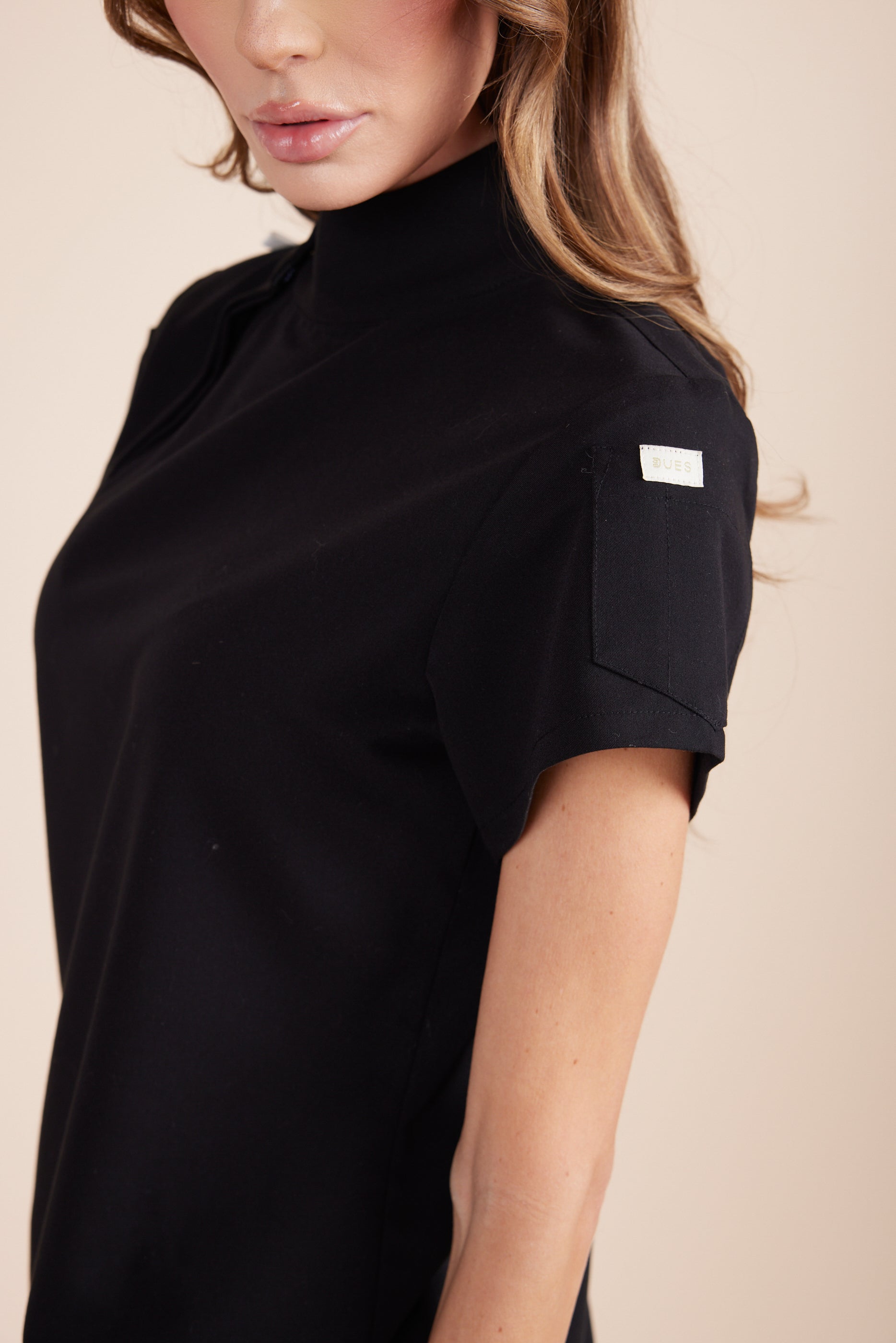Jackie Scrub Top in Black by DUES – luxury scrub top sewn in the USA, featuring contrast key loops, side splits, and high-stretch panels for comfort and mobility.