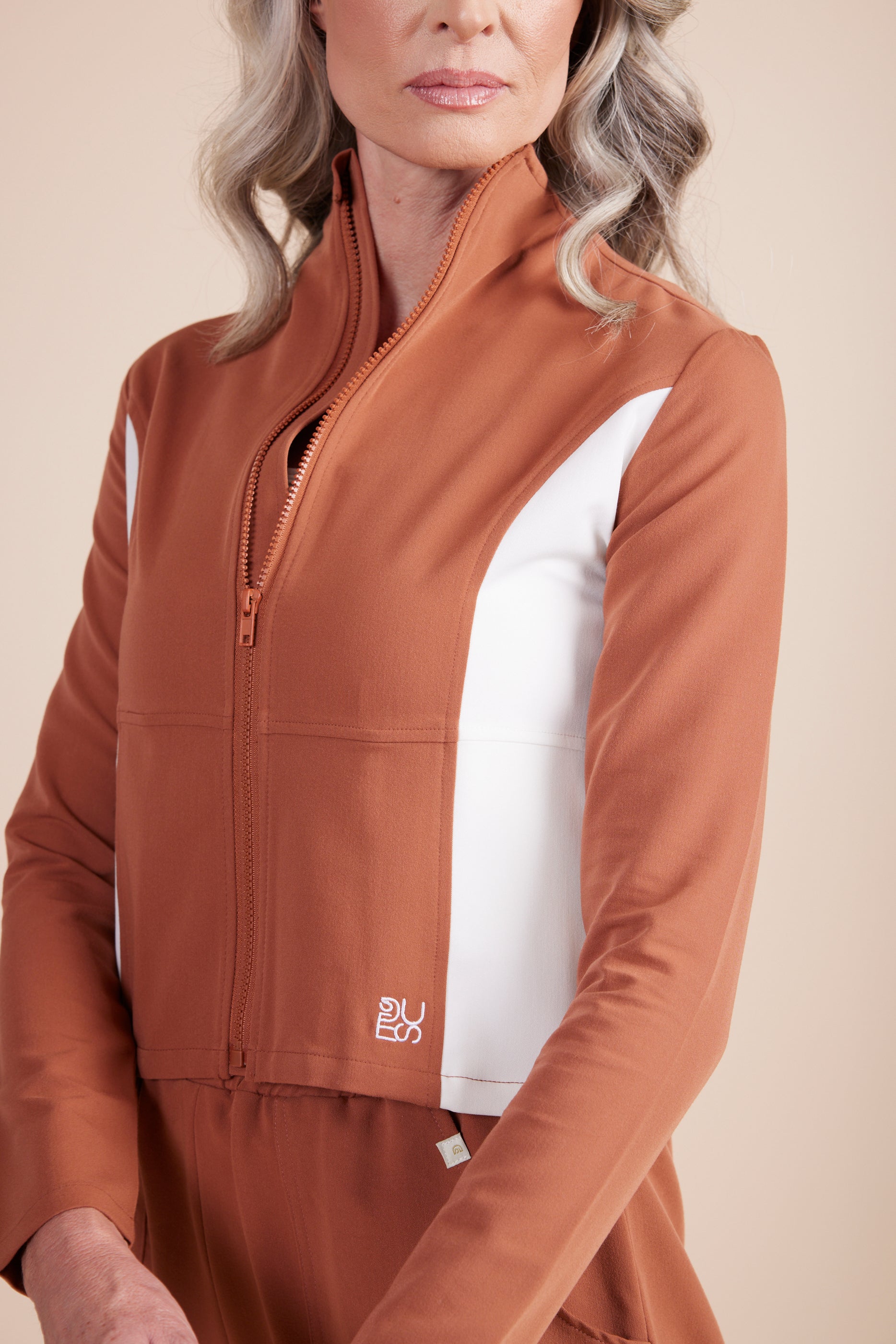Jade Jacket in Terracotta by DUES – luxury zip-up scrub jacket sewn in the USA, featuring contrast white side panels, a sleek high collar, and modern tailoring for a polished, functional fit.