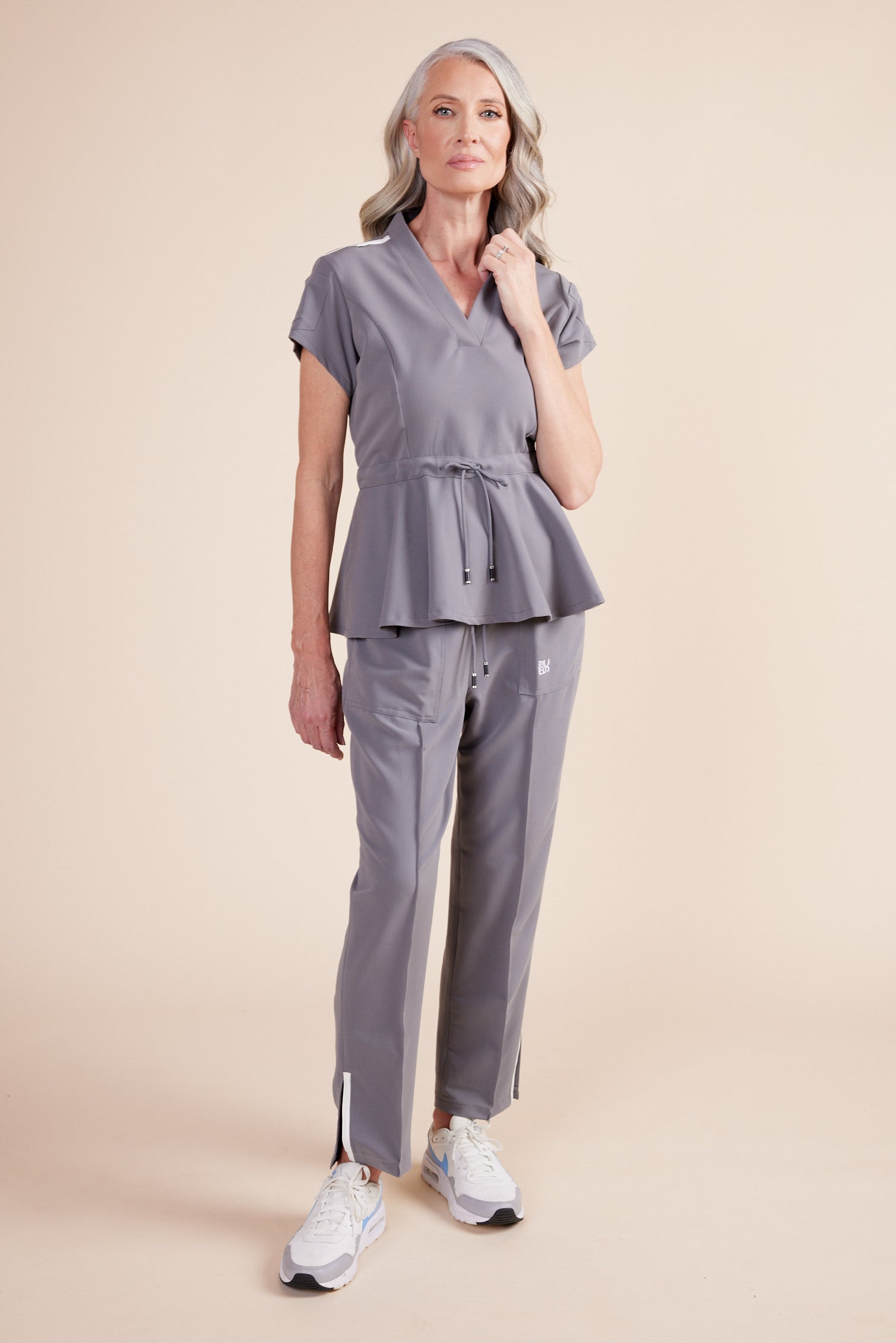 Deanna Scrub Top in Gray by DUES – luxury scrub top sewn in the USA, featuring a cinched waist design, contrast key loops, side splits, and high-stretch panels for comfort and mobility.