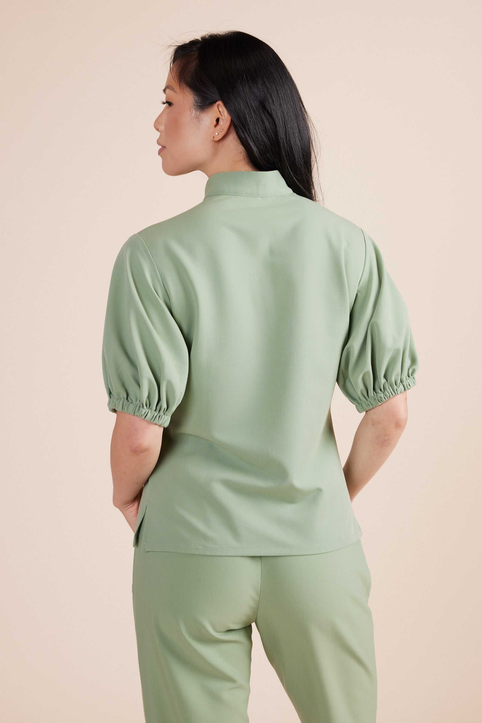 Helen Scrub Top in Green Tea by DUES – luxury scrub top sewn in the USA, featuring contrast key loops, side splits, and high-stretch panels for comfort and mobility.